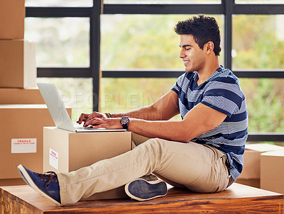 Buy stock photo Shot of a young man using a laptop while taking a break from moving into a new home