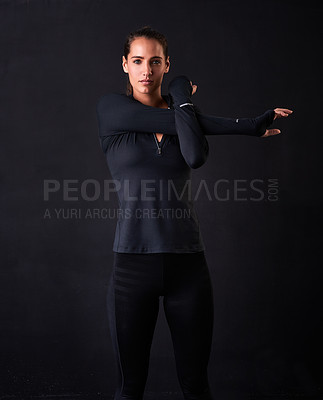 Buy stock photo Studio portrait of a young woman in gym clothes stretching her arms against a dark background