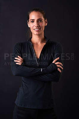 Buy stock photo Studio portrait of a young woman in gym clothes standing with her arms crossed against a dark background
