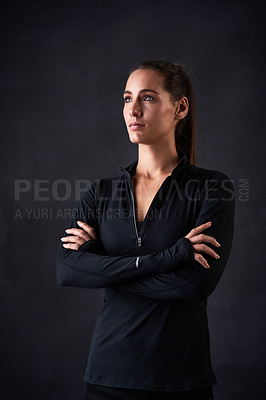 Buy stock photo Studio shot of a young woman in gym clothes standing with her arms crossed against a dark background