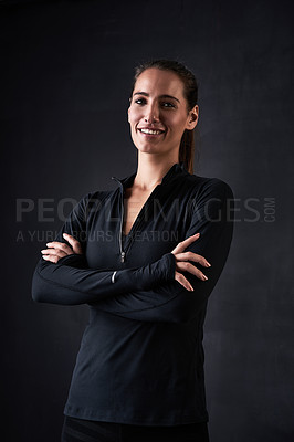 Buy stock photo Studio portrait of a young woman in gym clothes standing with her arms crossed against a dark background