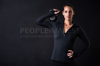Buy stock photo Studio portrait of a young woman in gym clothes holding a kettlebell against a dark background