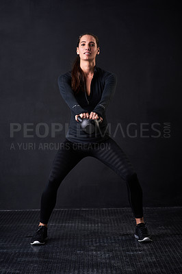 Buy stock photo Studio portrait of a young woman in gym clothes working out with a kettlebell against a dark background