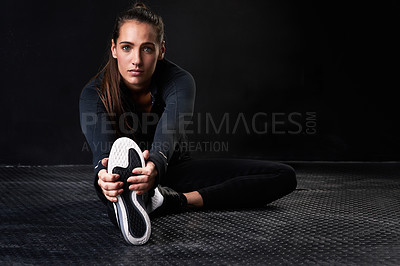 Buy stock photo Studio portrait of a young woman in gym clothes stretching her legs against a dark background