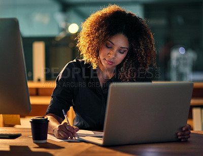 Buy stock photo Shot of a young businesswoman using a laptop and writing notes during a late night at work