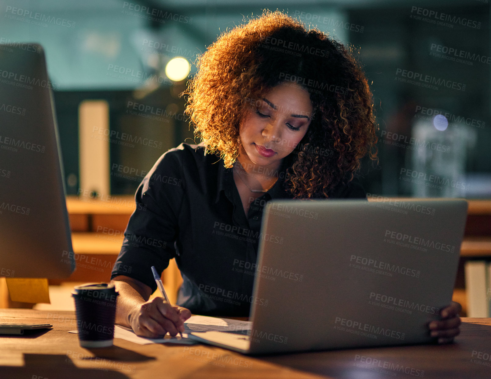 Buy stock photo Shot of a young businesswoman using a laptop and writing notes during a late night at work