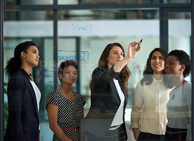 Buy stock photo Shot of a group of businesswomen working on a glass wall during a meeting