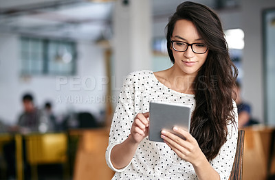 Buy stock photo Shot of a young woman using a digital tablet while sitting in a modern office