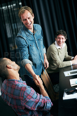 Buy stock photo Shot of two colleagues shaking hands in a boardroom while a coworker look on