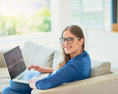 Buy stock photo Portrait of an attractive young woman using her laptop while sitting on the sofa at home