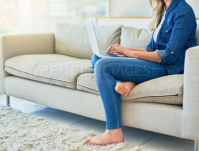 Buy stock photo Shot of an unrecognizable young woman using her laptop while sitting on the sofa at home