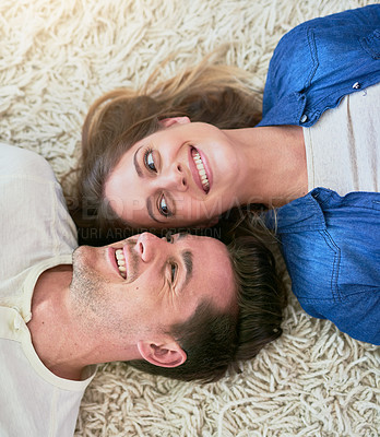 Buy stock photo High angle shot of an affectionate young couple lying on their living room floor