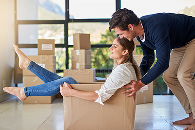 Buy stock photo Shot of a young man pushing his girlfriend around in a box while they move into their new home together