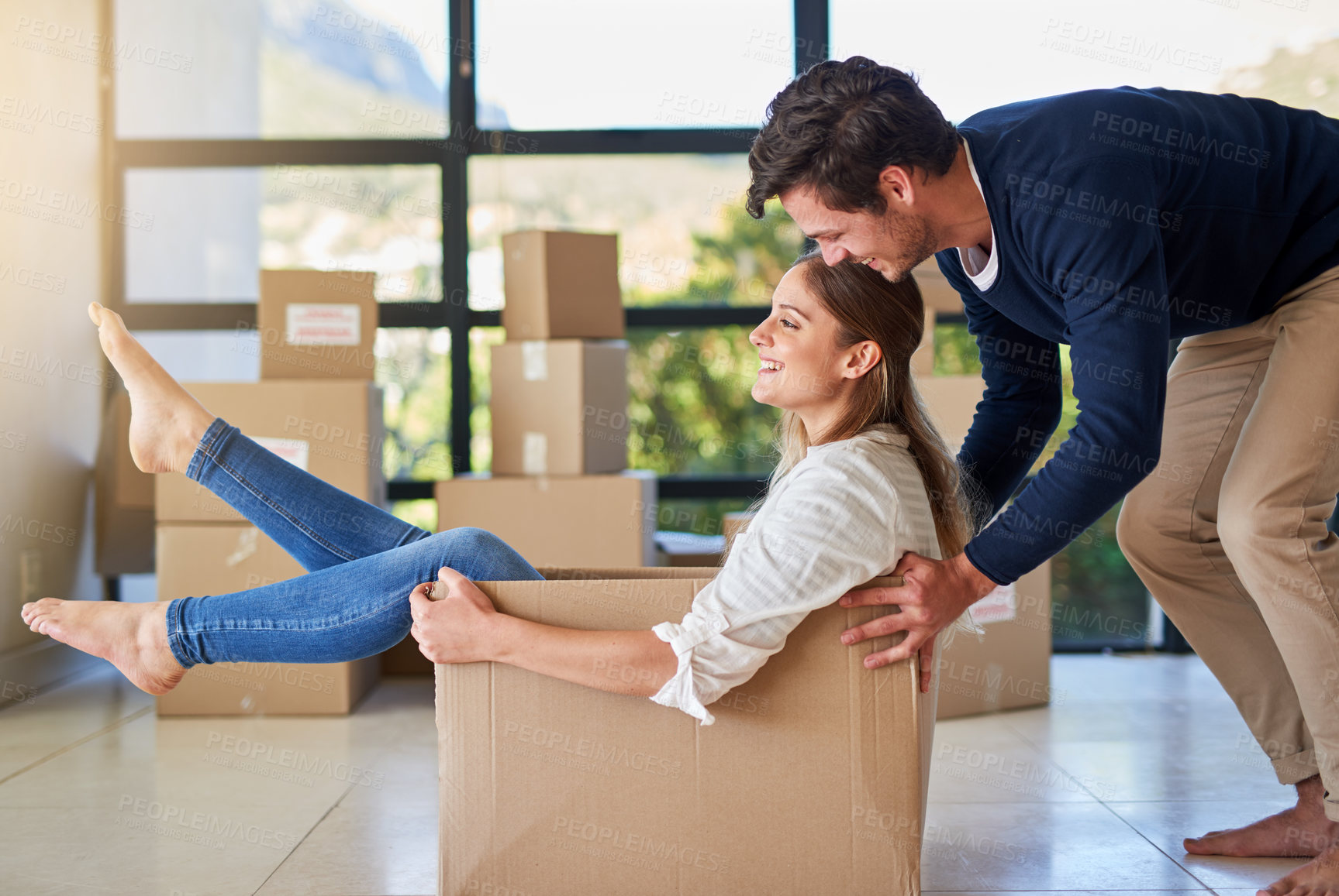 Buy stock photo Happy couple, box and moving in new home with fun for investment, property or apartment together. Young man pushing woman with boxes and playing in house for relocation, renovation or mortgage loan