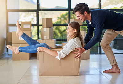 Buy stock photo Shot of a young man pushing his girlfriend around in a box while they move into their new home together