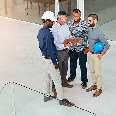Buy stock photo Shot of a group of male architects going over their plans while standing on site