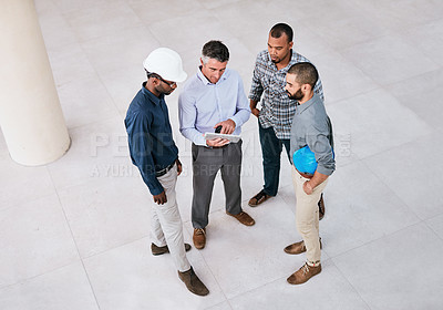 Buy stock photo Shot of a group of male architects looking at a tablet together while standing on site