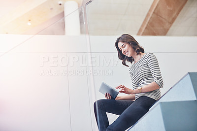 Buy stock photo Shot of a young designer using her tablet while sitting on the stairs in the office