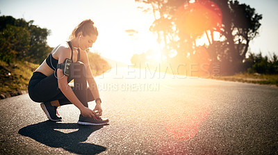 Buy stock photo Shot of a fit young woman tying her shoelaces before a run outdoors