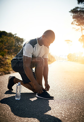 Buy stock photo Shot of a fit young man tying her shoelaces before a run outdoors