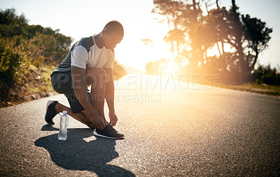 Buy stock photo Shot of a fit young man tying her shoelaces before a run outdoors