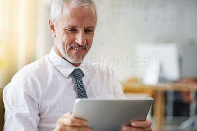 Buy stock photo Shot of a smiling mature businessman using a digital tablet while standing in an office
