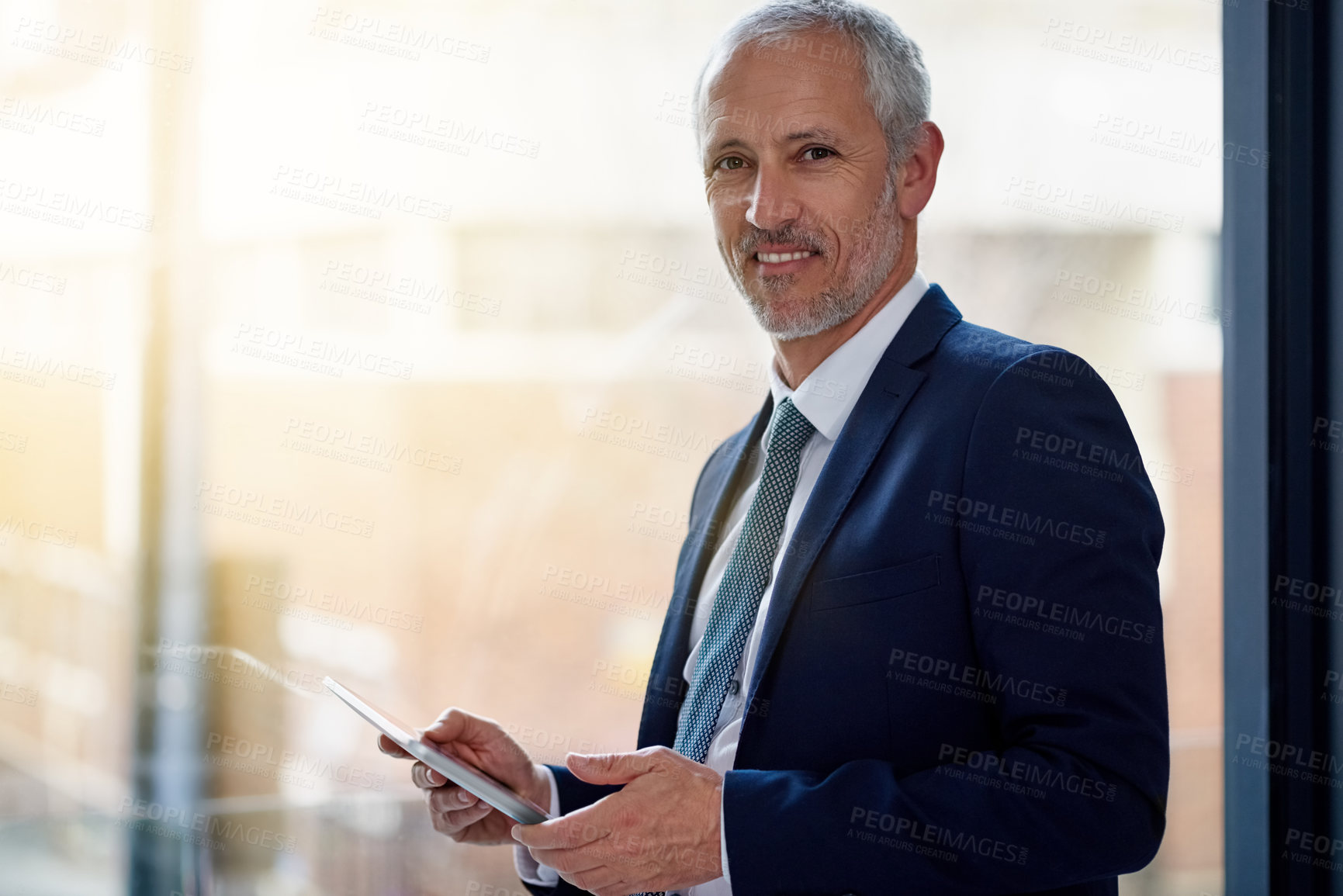 Buy stock photo Portrait of a smiling mature businessman using a digital tablet while standing in an office
