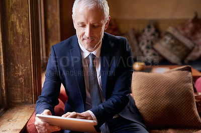 Buy stock photo Shot of a well-dressed mature man using a digital tablet in a cafe after work