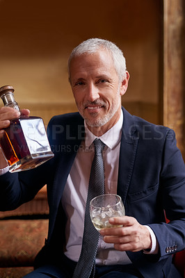 Buy stock photo Portrait of a well-dressed mature man holding a glass and whiskey bottle in a bar after work