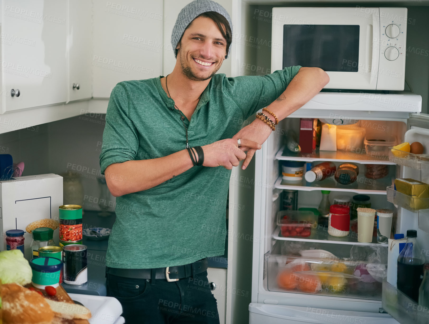 Buy stock photo Portrait of a smiling young man standing by an open fridge in his kitchen