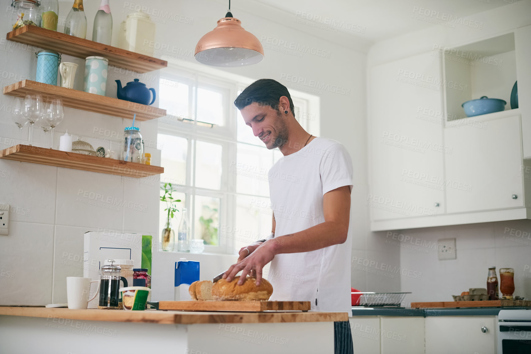 Buy stock photo Shot of a handsome young man standing in his kitchen making a sandwich