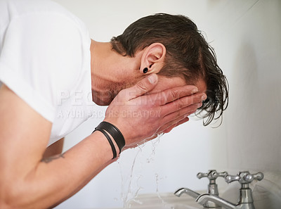 Buy stock photo Shot of a young man washing his face in a bathroom sink