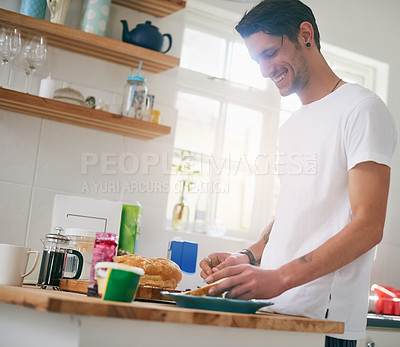 Buy stock photo Shot of a handsome young man standing in his kitchen making a sandwich