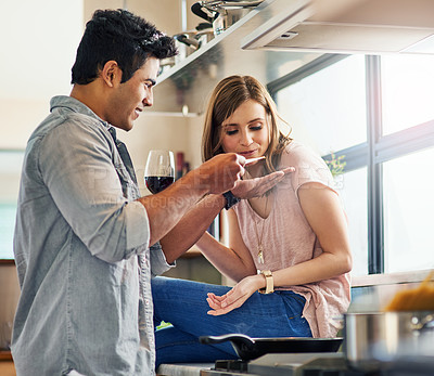 Buy stock photo Shot of a young man giving his wife a taste of the meal he's preparing