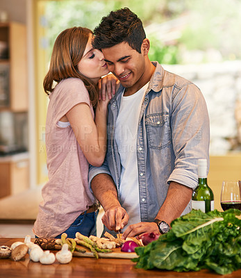 Buy stock photo Shot of a young woman kissing her husband while he prepares dinner