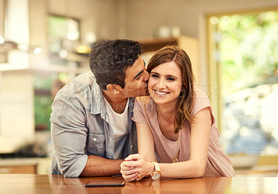 Buy stock photo Shot of an affectionate young man kissing his wife on the cheek in the kitchen