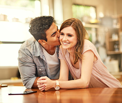 Buy stock photo Shot of an affectionate young man kissing his wife on the cheek in the kitchen