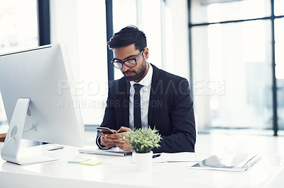 Buy stock photo Cropped shot of a young businessman using his cellphone at his desk