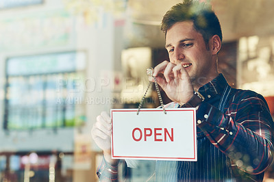 Buy stock photo Shot of a young man hanging up an open sign in a shop window