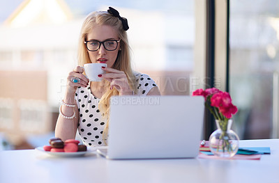 Buy stock photo Shot of a creative young businesswoman drinking coffee while using her laptop in the office
