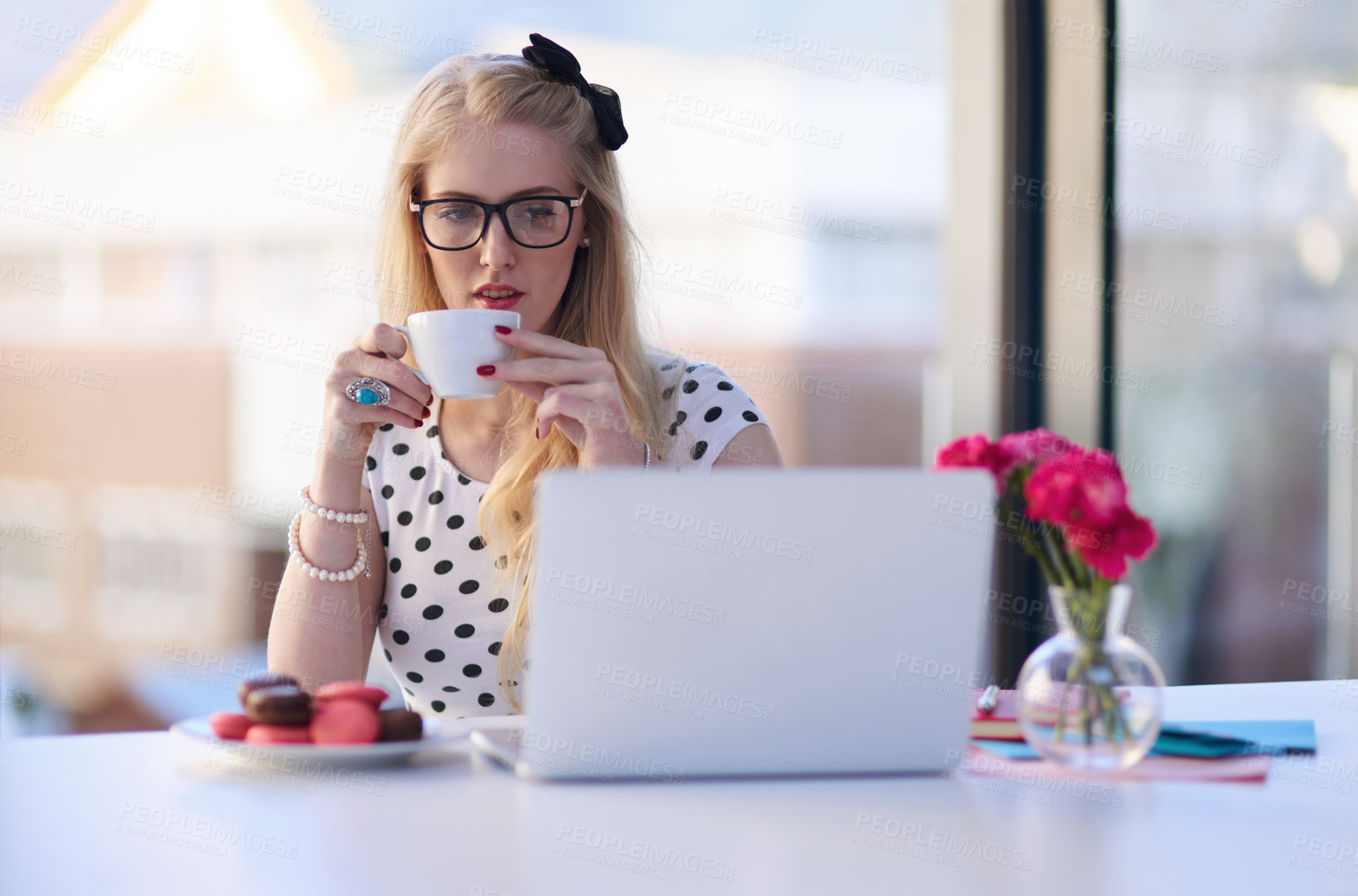 Buy stock photo Shot of a creative young businesswoman drinking coffee while using her laptop in the office