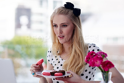 Buy stock photo Shot of a creative young businesswoman eating macarons while using her laptop in the office