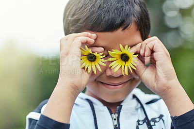 Buy stock photo Shot of a little boy holding to flowers up in front of his eyes while playing outside