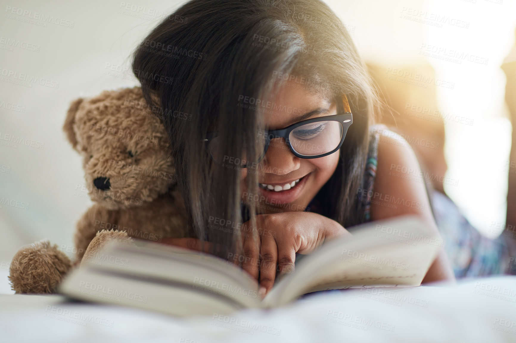 Buy stock photo Shot of a cute little girl reading a book in her bedroom with her teddybear by her side