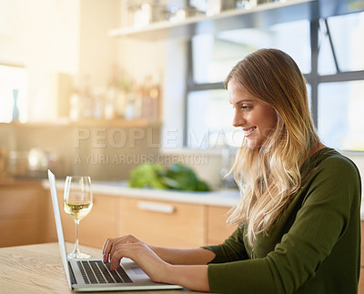 Buy stock photo Shot of an attractive young woman using laptop on her kitchen counter at home