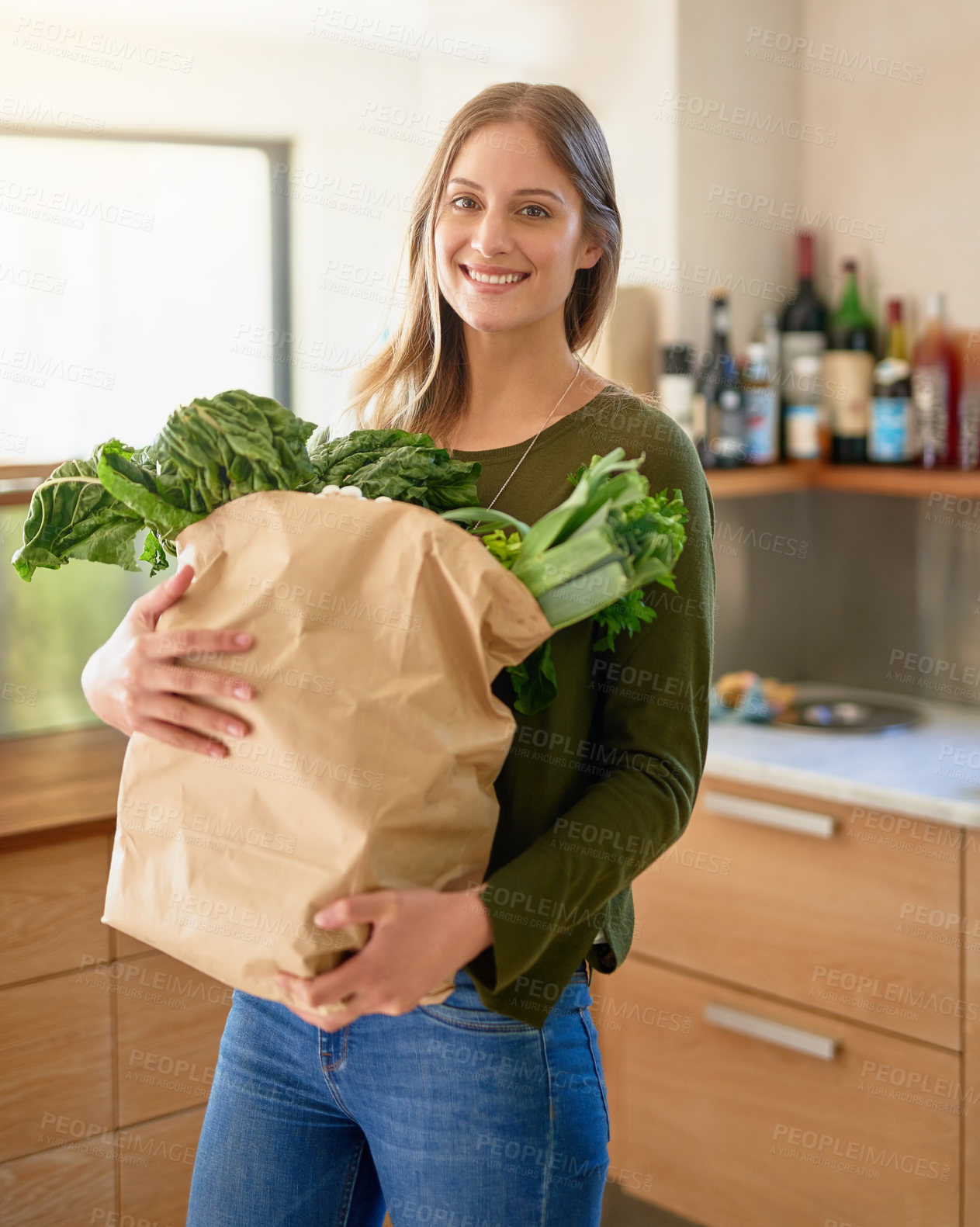 Buy stock photo Portrait of a smiling young woman standing in her kitchen carrying a paper bag full of groceries