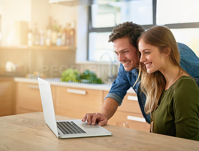 Buy stock photo Shot of a smiling young couple using laptop on their kitchen counter at home
