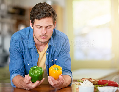 Buy stock photo Shot of a young man deciding which kind or pepper to cook with while standing in the kitchen at home