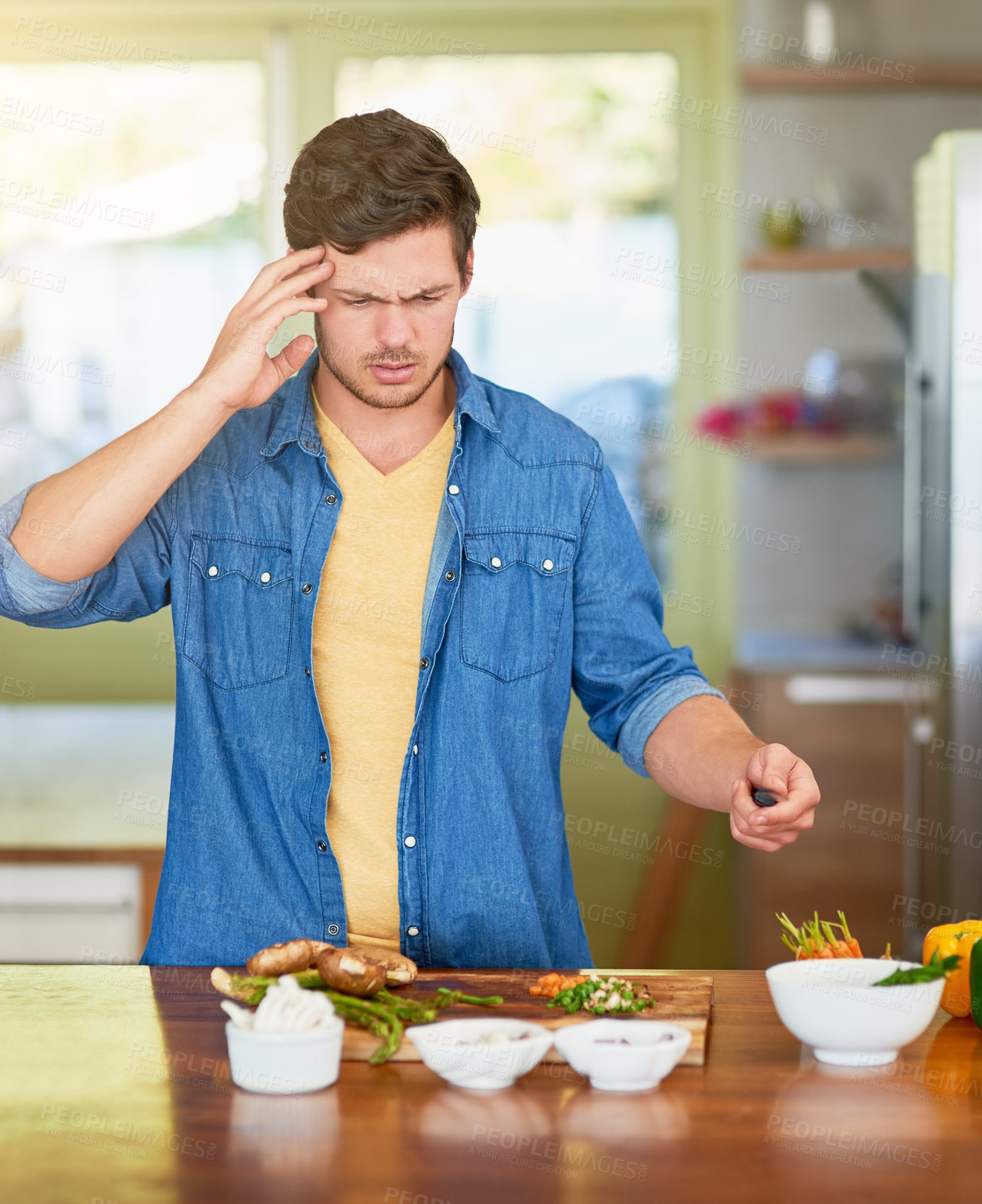 Buy stock photo Shot of a confused young man looking at recipe ingredients on a kitchen counter at home
