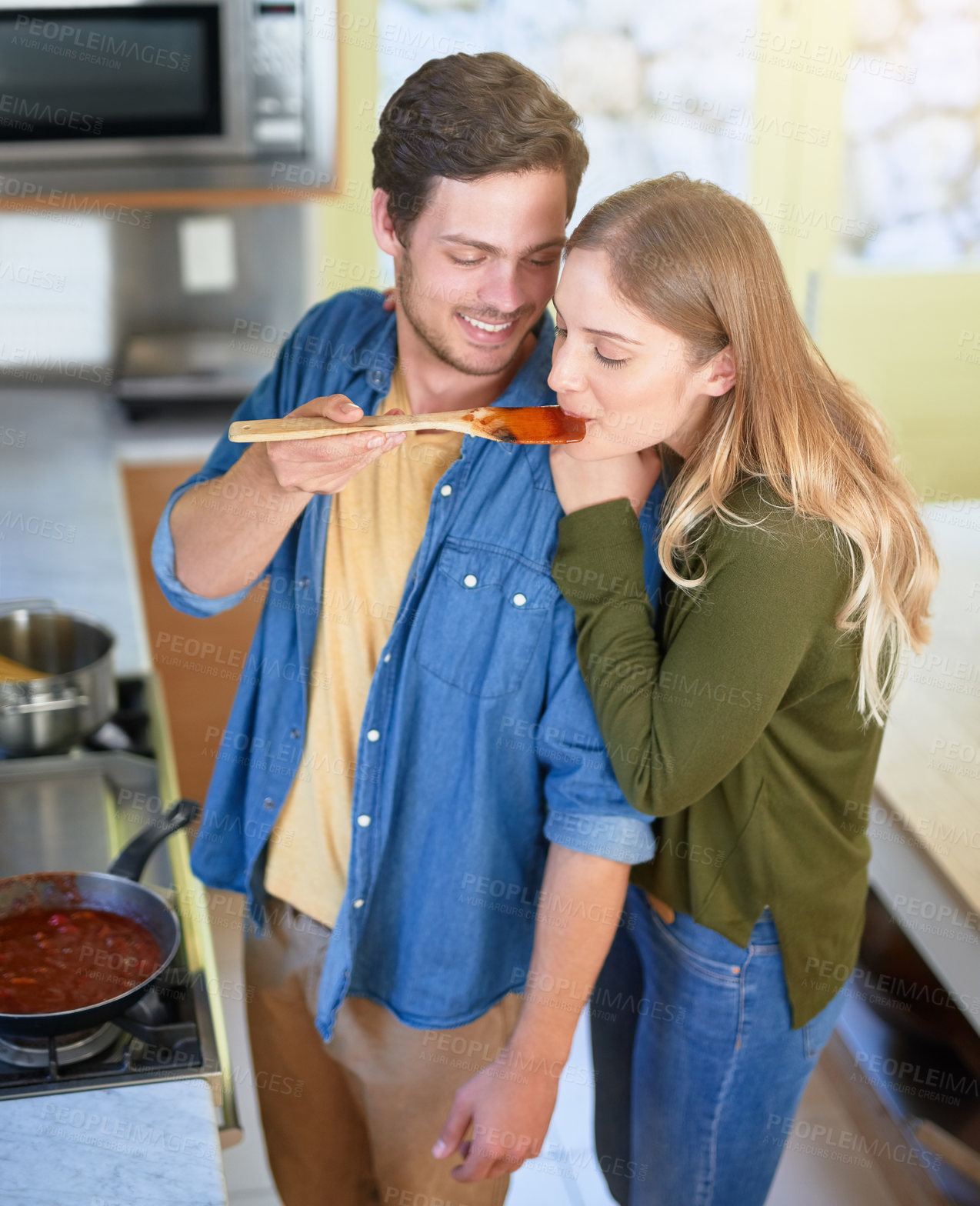 Buy stock photo Shot of an affectionate young couple tasting a sauce they are preparing together in their kitchen